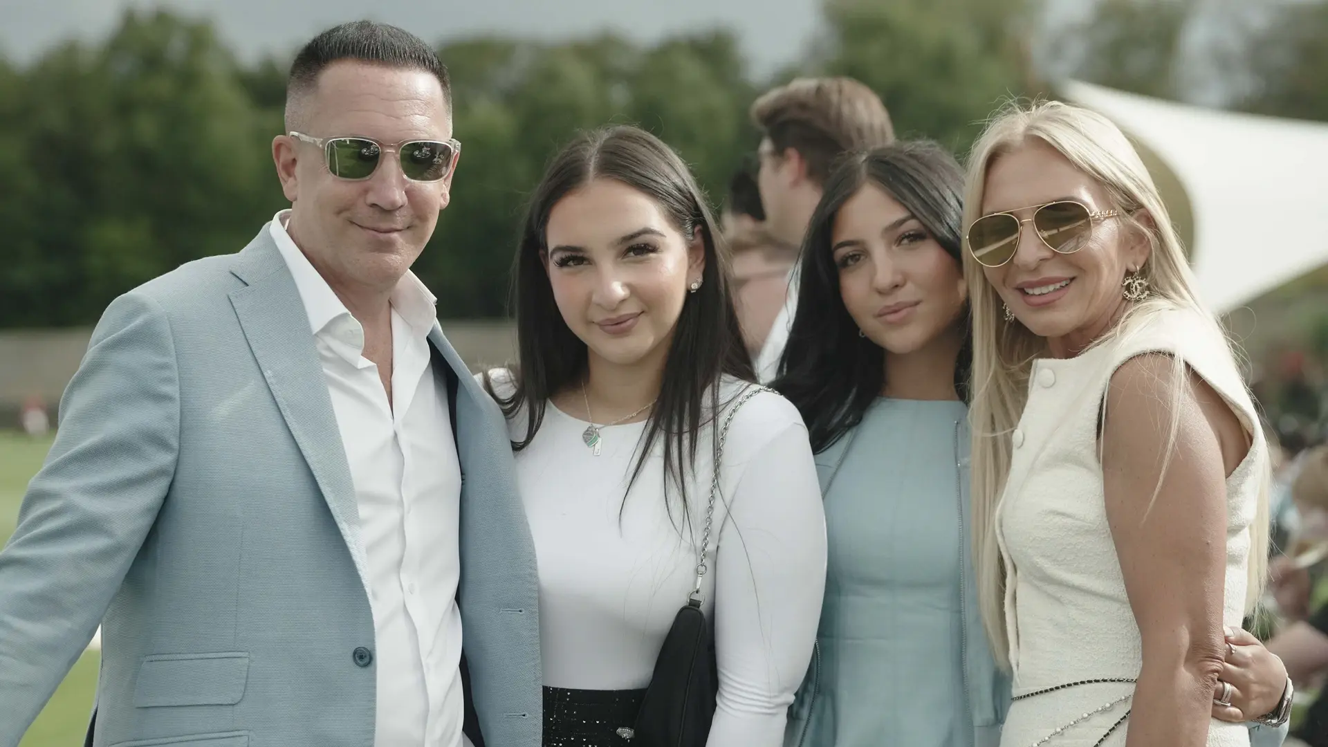 Familie Kundler posiert gemeinsam für ein Foto beim Maifeld Polo Cup 2025 und steht eng beieinander vor einem weich, unscharfen grünen Im Freien Hintergrund